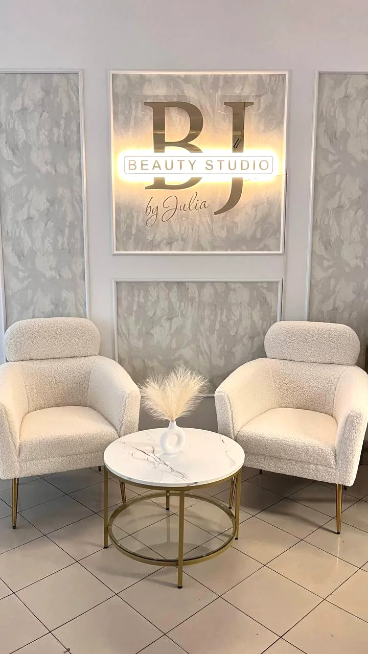 Skutečný interiér BJ Beauty – elegantní světlá křesla a zlaté logo